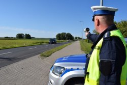 Policjant WRD podczas kontroli prędkości jazdy kierowców w m. Stary Widzim. W tle dwa auta jadące w kierunku policjanta.