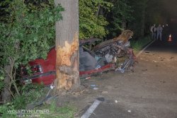 Miejsce wypadku - droga w 313. Na pierwszym planie uszkodzony pojazd i drzewo, w które uderzył kierowca. W tle sylwetki dwóch osób w maseczkach.