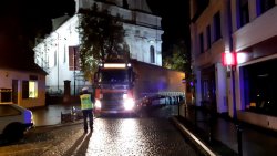 Ciągnik siodłowy marki Volvo z naczepą utknął na wąskiej ulicy. Policjant Wydziału Ruchu Drogowego umożliwia kierowcy wyjazd w kierunku Rynku i ulicy Poznańskiej.