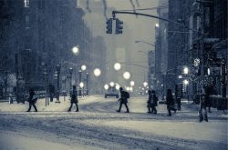 Ulica dużego miasta podczas śnieżycy. Ludzie idący jeden za drugim przechodzą na drugą stronę ulicy.