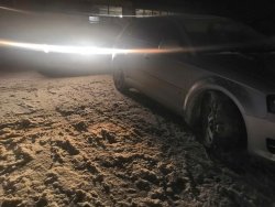 Sceneria nocna. Na zaśnieżonym podłożu stoi samochód osobowy koloru srebrnego, za nim radiowóz oznakowany nadający sygnały świetlne. Widoczne światła radiowozu i napis POLICJA na górnej belce