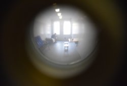 Pomieszczenie policyjnego aresztu widziane przez wizjer. W pomieszczeniu widoczna sylwetka mężczyzna siedzącego na pryczy.