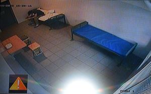 Pomieszczenie dla osób zatrzymanych KPP w Wolsztynie. Podejrzewany o udział w kradzieży mężczyzna siedzi na pryczy. Jest pochylony do przodu. Po prawej stronie druga prycza, po lewej stolik, dwa taborety i fragment drzwi.