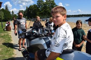 Akcja profilaktyczna &quot;Kręci mnie bezpieczeństwo nad wodą&quot; nad jeziorem Wieleńskim. Chłopiec siedzi na policyjnym motocyklu.