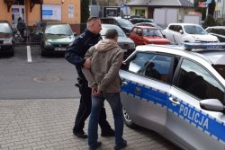 Policjant umieszcza zatrzymanego w radiowozie. Konwój do prokuratury.