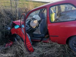 Stojący w rowie, uszkodzony w wyniku wypadku nissan micra, &quot;wystrzelone&quot; poduszki powietrzne. W tle funkcjonariusze straży pożarnej.