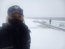 Sceneria zimowa - śnieg i lód. Zdjęcie typu selfie. Policjantka na pierwszym tle, widoczny imiennik z nazwiskiem KUCHARCZAK. W oddali na pomoście dzielnicowy.