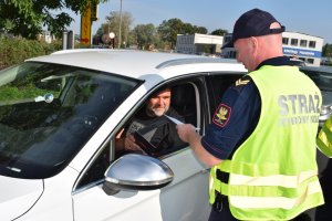 Akcja &quot;Bezpieczny przejazd&quot;. Strażnik Ochrony Kolei wręcza kierowcy białego auta osobowego ulotkę informacyjną.