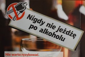 Hasło kampanii NIGDY NIE JEŻDŻĘ PO ALKOHOLU. W tle kieliszek z alkoholem, poniżej napis NIE WARTO RYZYKOWAĆ