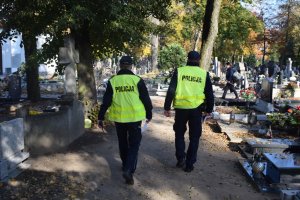 Policjanci podczas patrolu wykonywanego w obrębie cmentarza w Wolsztynie. Na drugim planie ludzie podczas porządkowania grobów.