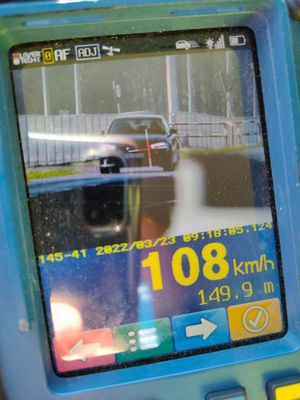 Ekran miernika prędkości wskazujący 108 km/h. W tle samochód sprawcy wykroczenia.