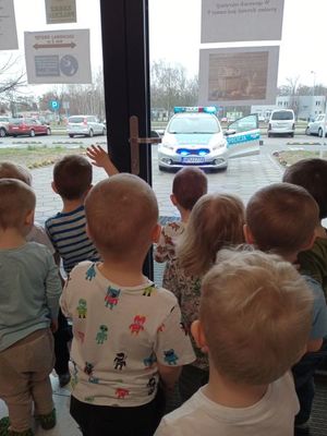 Dzieci stoją przy przeszklonych drzwiach obserwując radiowóz podczas nadawania sygnałów świetlnych