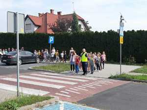 Akcja &quot;Pomachaj kierowcy&quot;. Policjantka podczas zajęć praktycznych z dziećmi przechodzi przez oznakowane przejście dla pieszych przy Szkole Podstawowej nr 5 w Wolsztynie.