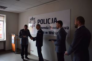 Uroczystość pożegnania przechodzącego na emeryturę komisarza Rafała Płóciniczaka. Komendant w towarzystwie Zastępcy Naczelnika Wydziału Prewencji odczytuje list gratulacyjny.