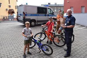 Stojący na tle radiowozu policjant i czworo uczestników akcji znakowania ze swoimi rowerami.