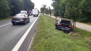 Widok na drogę. Sznur pojazdów poruszających się w obu kierunkach. Po prawej stronie, w rowie uszkodzony w kolizji samochód - czarny Volkswagen Golf.