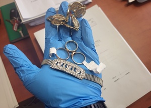 Policjant eksponuje zabezpieczoną biżuterię - złote pierścionki i bransolety trzymając je w otwartej dłoni.