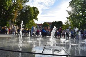 Akcja ODBLASKOWY MALUCH zorganizowana na wolsztyńskim Rynku. Na pierwszym planie rozbryzgujące się strumienie wody z fontanny, w oddali dzieci zgromadzone na Rynku.