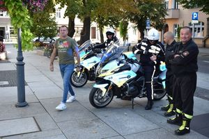Akcja ODBLASKOWY MALUCH zorganizowana na wolsztyńskim Rynku. Dwaj policjanci Wydziału Ruchu Drogowego na motocyklach. Obok dwaj strażacy i pracownik Wolsztyńskiego Domu Kultury.