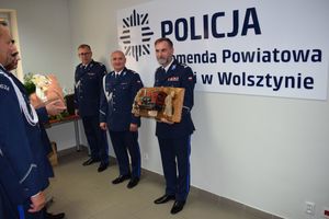 Ustępujący Komendant Powiatowy Policji w Wolsztynie prezentuje trzymany w rękach upominek - model lokomotywy przytwierdzony do drewnianej konstrukcji, przekazany przez naczelników KPP w Wolsztynie.