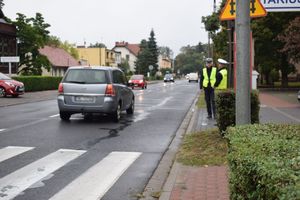 Dwaj umundurowani policjanci służby ruchu drogowego kontrolują ruch pieszy i kołowy w rejonie przejścia dla pieszych na ul. Poniatowskiego w Wolsztynie.