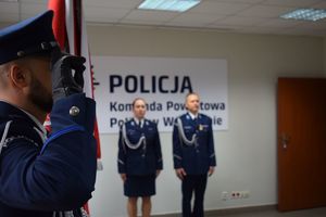 Sala Konferencyjna KPP w Wolsztynie. Po lewej stronie stoi salutujący policjant wchodzący w skład pocztu sztandarowego na wprost Komendant i Zastepca Komendanta Powiatowego Policji w Wolsztynie