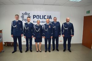 Sala Konferencyjna KPP w Wolsztynie.  I Zastępca Komendanta Powiatowego Policji w Wolsztynie pozuje do zdjęcia z gośćmi uroczystej zbiórki.