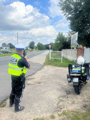 Stojący przy motocyklu policjant mierzy prędkość pojazdów na drodze
