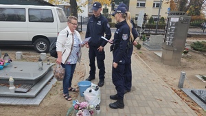 Policjanci rozmawiają na cmentarzu z ludźmi porządkującymi groby oraz wręczają im ulotki z poradami dotyczącymi bezpieczeństwa.