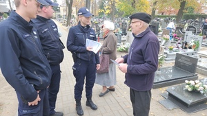 Policjanci rozmawiają na cmentarzu z ludźmi porządkującymi groby oraz wręczają im ulotki z poradami dotyczącymi bezpieczeństwa.