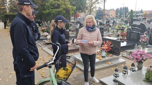 Policjanci rozmawiają na cmentarzu z ludźmi porządkującymi groby oraz wręczają im ulotki z poradami dotyczącymi bezpieczeństwa.