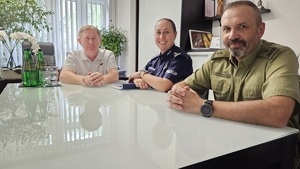 Gabinet dyrektora szkoły. Przy stole o białym blacie siedzą trzy osoby uczestniczące w spotkaniu - kobieta i dwaj mężczyźni.