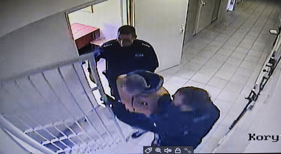 Korytarz policyjnego aresztu. Policjanci wyprowadzają zatrzymanego.