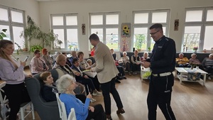 Debata społeczna w Domu Dziennym Senior+. Naczelnik Wydziału Ruchu Drogowego oraz reprezentant Urzędu Miasta w Wolsztynie przekazują seniorom elementy odblaskowe.